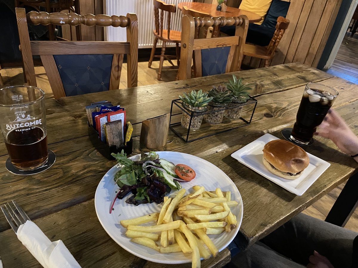 A burger and chips on a scrubbed wooden table beside a glass of Butcombe ale.