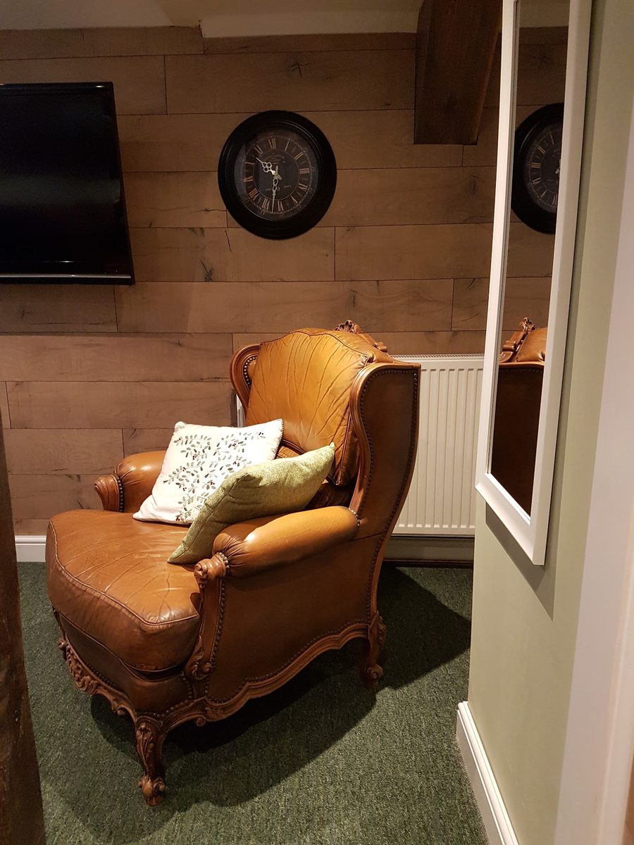 A guest lounge with a tan leather armchair against a panelled oak wall.