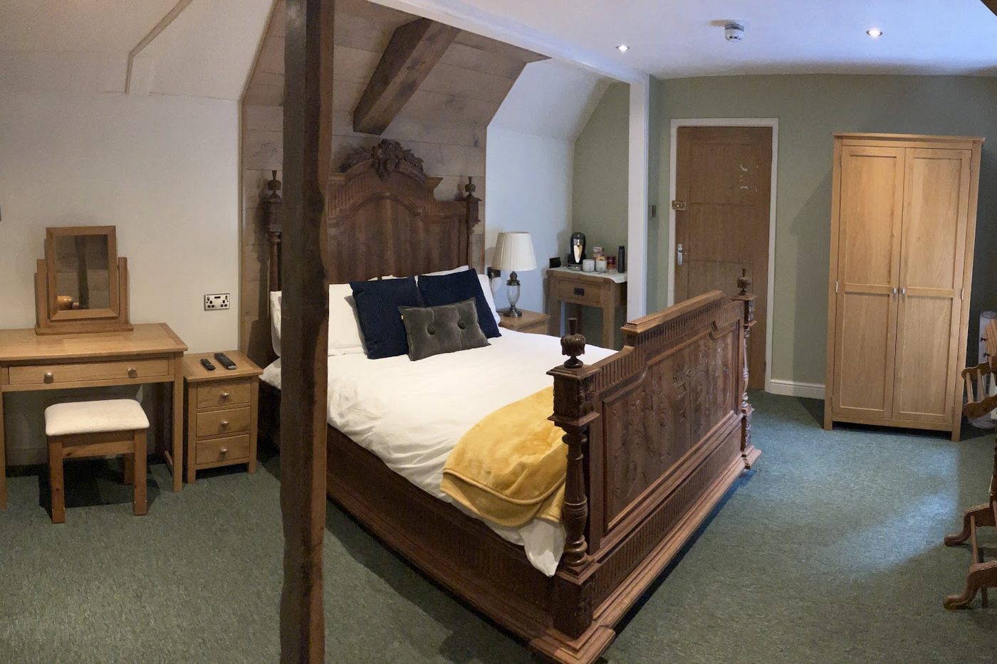 A letting room with a carved four-poster bed, oak wardrobe, dressing table and a tea and coffee tray.