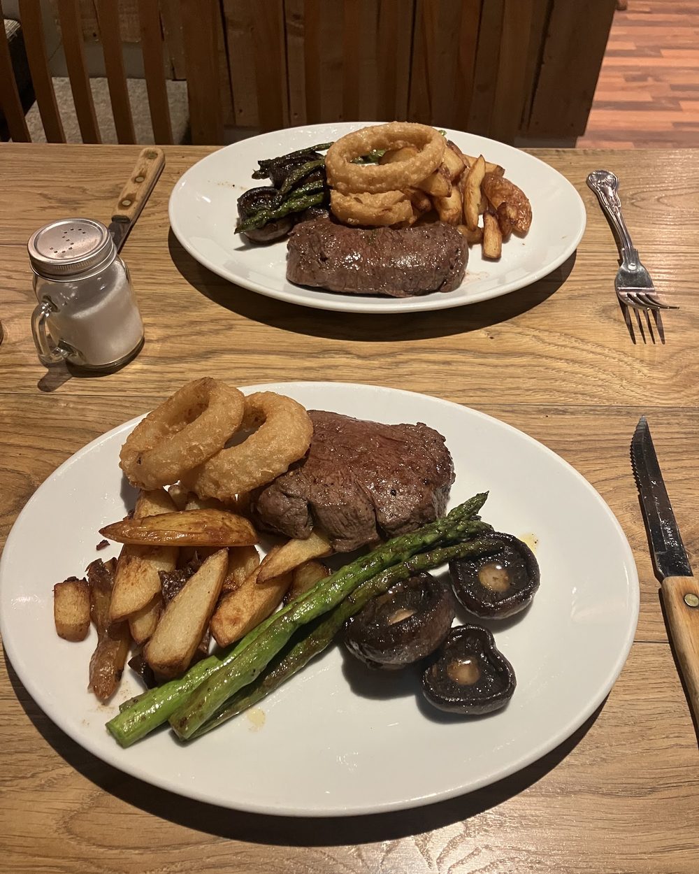 A steak with hand-cut chips, onion rings, asparagus and flat mushrooms on a white plate.